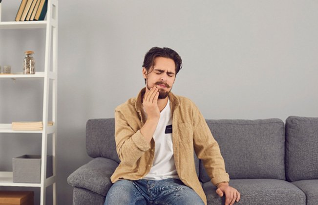 a dental patient sitting at home and holding his jaw