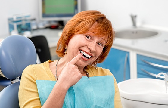 Red-haired senior female dental patient pointing to her smile