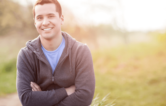 Man in jacket smiling outside with arms folded